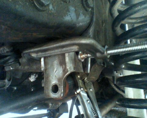 1987 Ford Bronco - A mechanic works on a vehicle's suspension system, focusing on a metal bracket and coil spring.