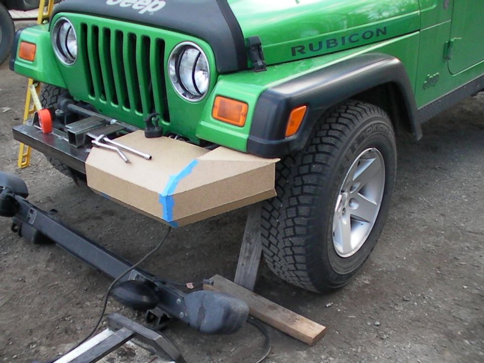 Green Jeep Wrangler with 'Rubicon' decal, front bumper being modified with cardboard template and tools