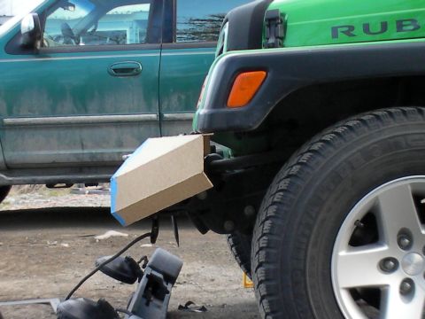 1987 Suzuki Samurai - A green Jeep Wrangler's front bumper is fitted with a cardboard prototype, partially obscured by a green SUV.