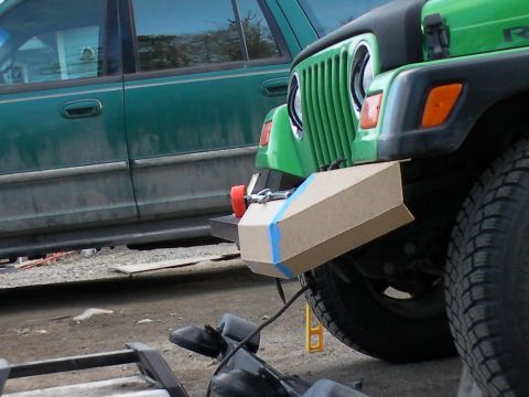 1987 Suzuki Samurai - A green Jeep Wrangler's front bumper is fitted with a cardboard attachment secured by blue tape, with another green vehicle visible behind…