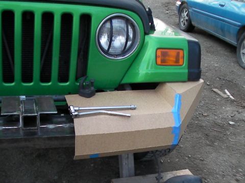 1987 Suzuki Samurai - A cardboard template is taped to the front bumper of a green Jeep Wrangler, with a blue car visible in the background.