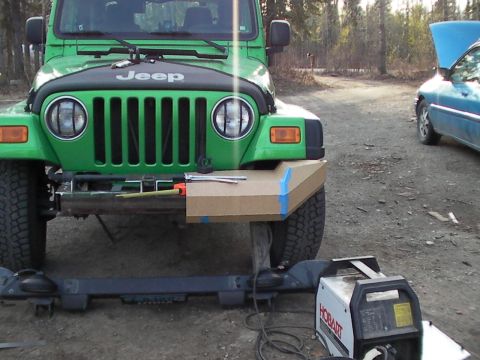 1987 Suzuki Samurai - Custom bumper fabrication in progress on a green Jeep Wrangler, with a blue car in the background.