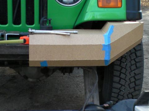 1987 Suzuki Samurai - A cardboard mockup is taped to the front of a green Jeep, obscuring the bumper area.