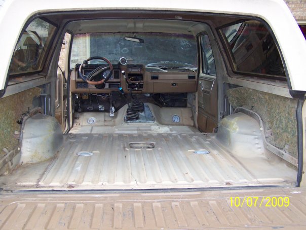 Stripped Bronco interior from rear tailgate, bare metal floor, brown dash and steering wheel visible