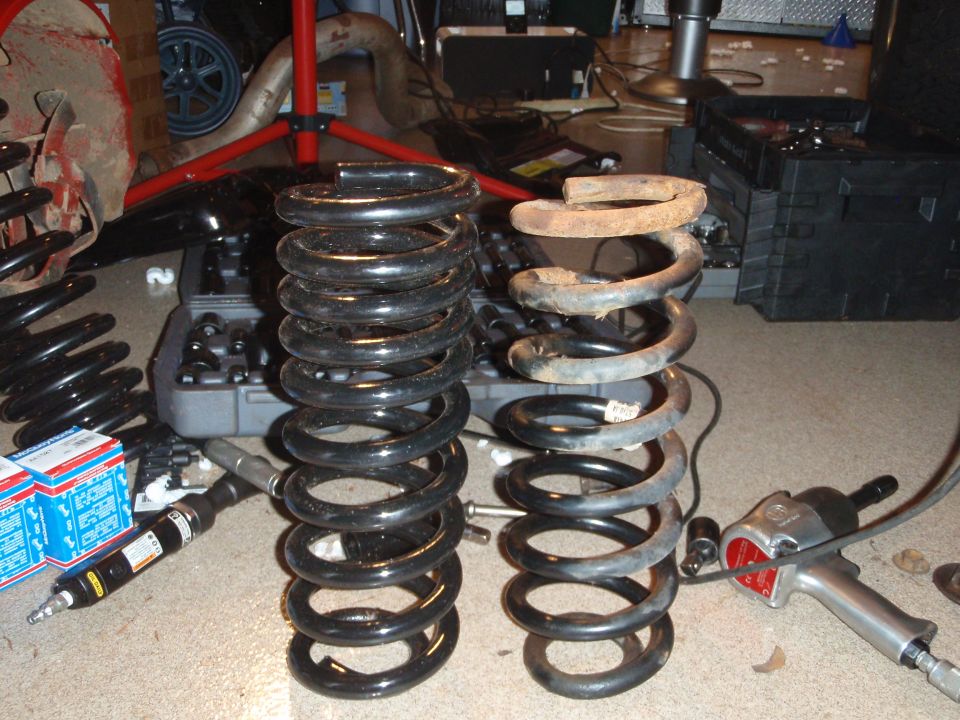 Two suspension springs, one new and one rusty, sit next to an impact wrench and tool case