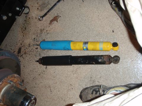 1995 Ford Bronco - A new yellow and blue shock absorber is compared to an old, rusty black one on a garage floor.
