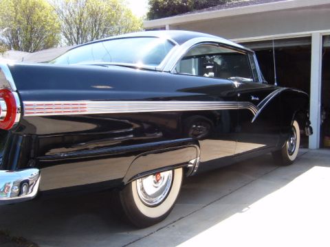 1956 Ford Fairlane - A classic black 1956 Ford Fairlane coupe is parked in a driveway, its distinctive chrome accents and whitewall tires.
