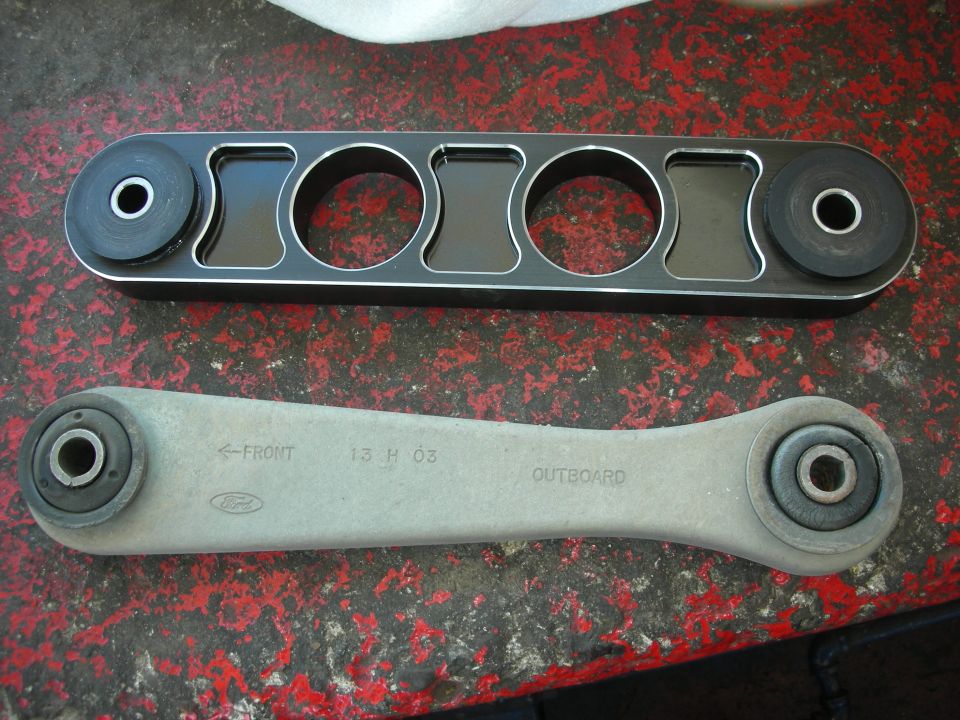 Two automotive rear control arm links, one billet aluminum and one stamped steel, marked Ford FRONT OUTBOARD 13 H 03