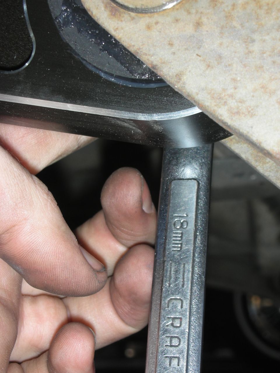 Hand bracing an 18mm Craftsman combination wrench against a vehicle suspension component
