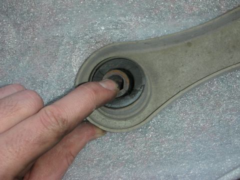 2004 Ford Crown Victoria - A finger points to a hex bolt head on a vehicle control arm part.