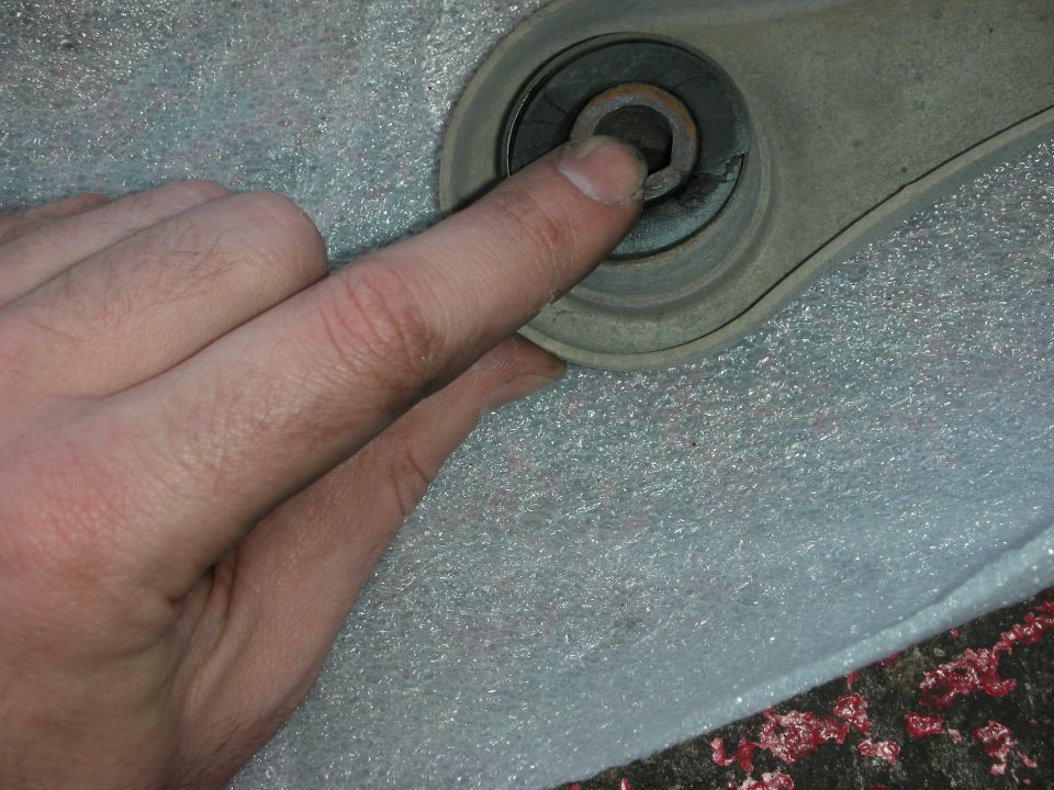 Hand pointing to a worn control arm bushing with a hex bolt head visible