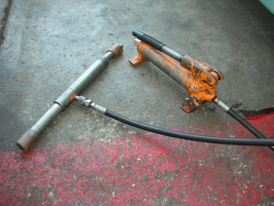 Orange hydraulic press and metal tool with hose on concrete floor