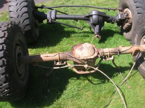 1996 Ford Bronco - Two vehicle axles with tires are displayed on a grassy lawn, one appearing rusty and the other painted black.