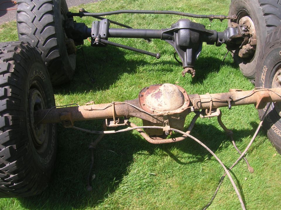 Two vehicle axles with tires, one rusty, one black, on grass