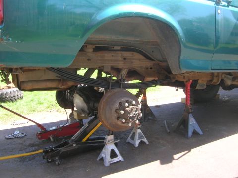 1996 Ford Bronco - The rear suspension of a green truck is disassembled and supported by jack stands.