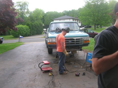 1996 Ford Bronco - A person in a welding mask works on the front end of a teal Ford truck in a driveway.