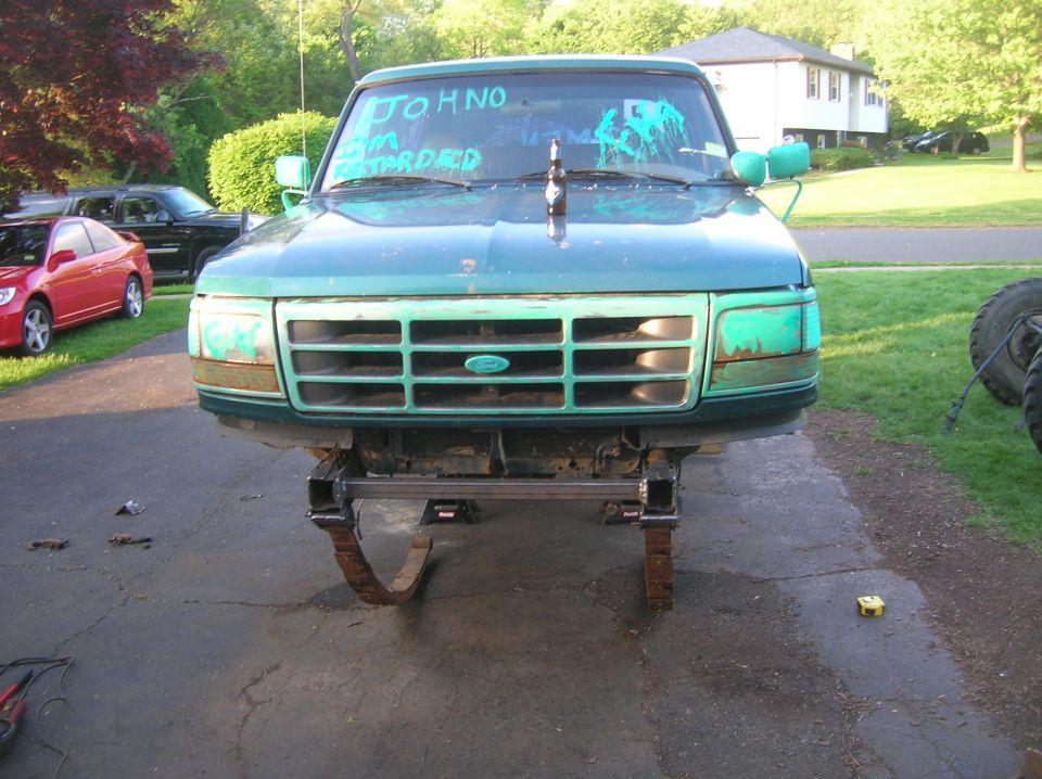 Green Ford truck with custom suspension, front view. Windshield has blue writing