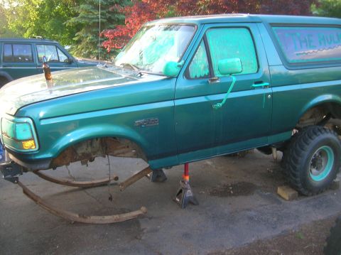 1996 Ford Bronco - A green 1996 Ford Bronco is seen on jack stands with its front suspension removed, and the text 'THE HULK' is visible on the rear window.