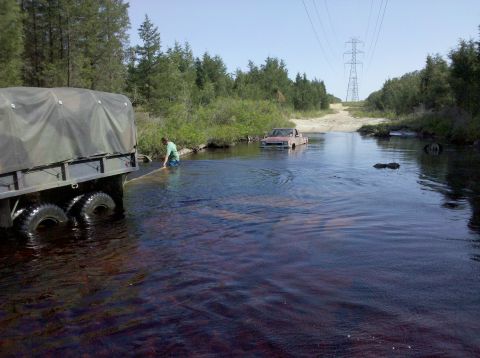 2005 Ford Excursion - A truck is partially submerged in a river while a person attempts to assist another vehicle in the background.