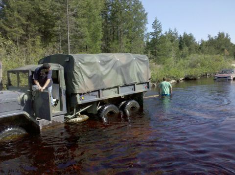 2005 Ford Excursion - A large military truck navigates through a shallow body of water, with a second vehicle partially submerged in the background.