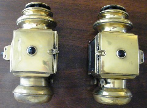 1912 Ford Model T - A pair of antique brass lanterns, likely for a vintage automobile, are displayed against a dark wood background.