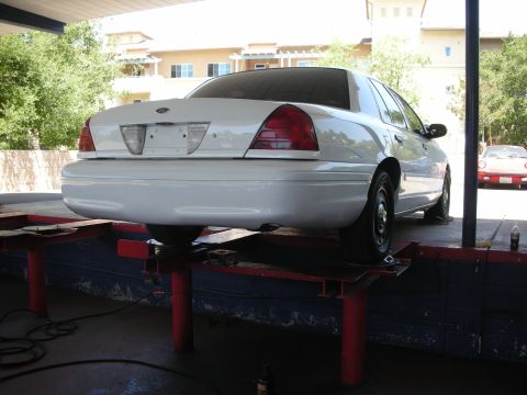 2004 Ford Crown Victoria - A white sedan is raised on a car lift, showing its undercarriage and rear end.