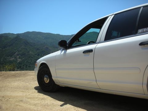 2004 Ford Crown Victoria - Side profile of a white 2004 Ford Crown Victoria parked on a dirt road with a mountainous landscape behind it.