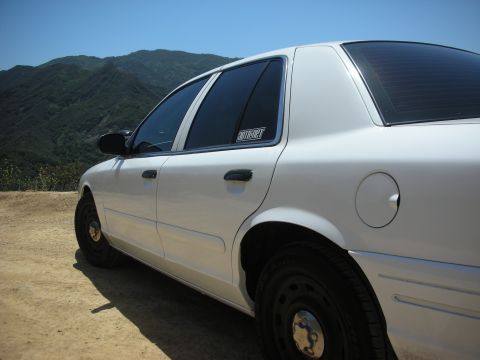 2004 Ford Crown Victoria - A white sedan is parked on a dirt road overlooking a mountainous landscape under a clear blue sky.