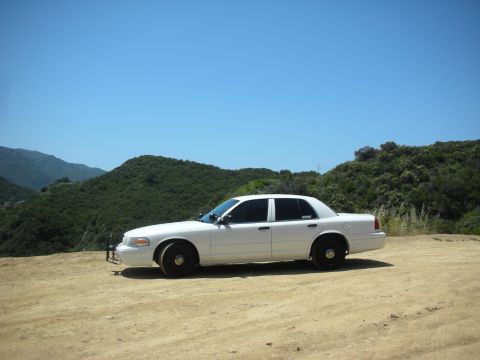 2004 Ford Crown Victoria - White 2004 Ford Crown Victoria parked on a dirt road with a hilly landscape.