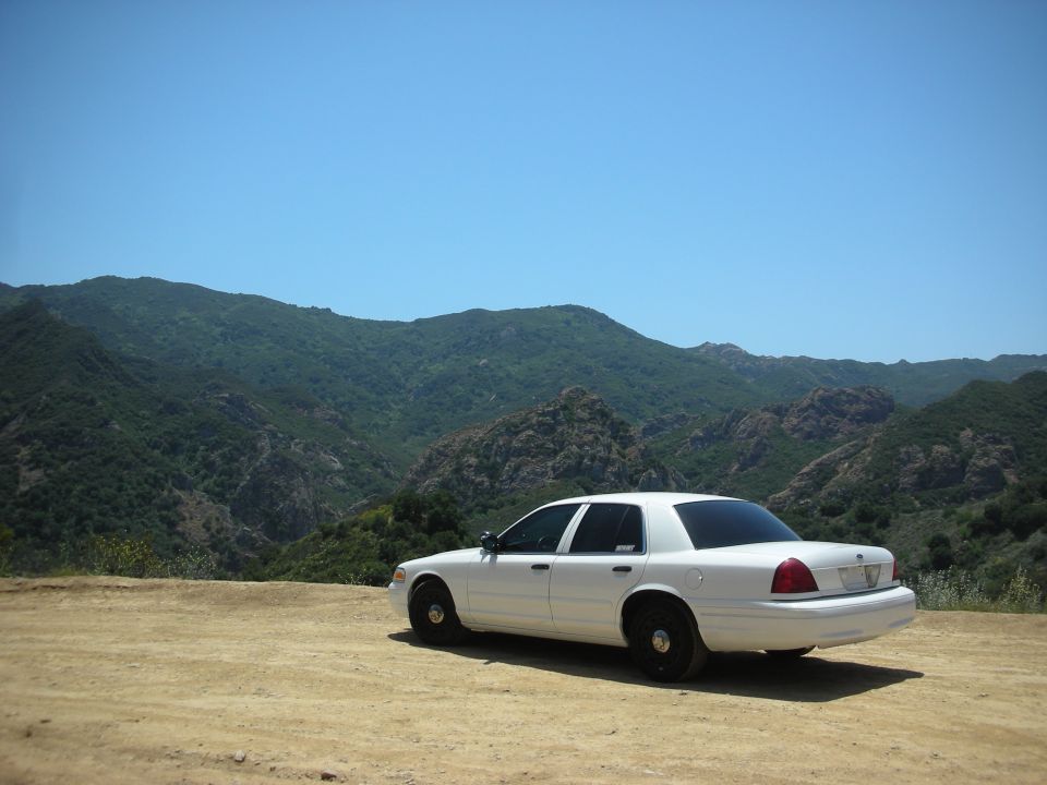 White 2004 Ford Crown Victoria parked on dirt road with mountains in background