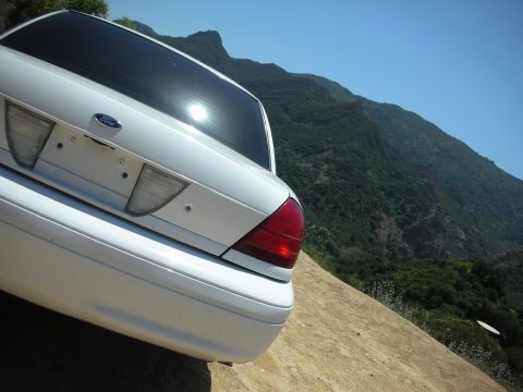 2004 Ford Crown Victoria - Rear view of a white Ford Crown Victoria parked on a dirt road with a mountainous landscape.
