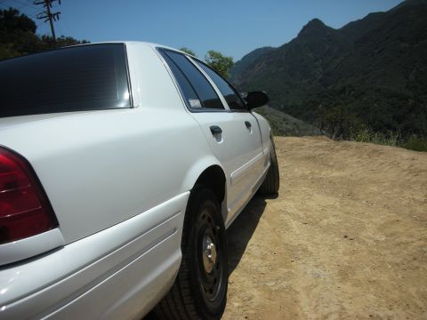 2004 Ford Crown Victoria - A white 2004 Ford Crown Victoria is parked on a dirt road overlooking a mountainous landscape.