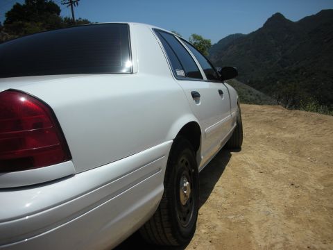 2004 Ford Crown Victoria - Side view of a white 2004 Ford Crown Victoria parked on a dirt road with a mountainous landscape.