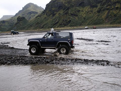 1996 Ford Bronco - A dark blue Ford Bronco navigates a rocky riverbed with other vehicles in the distance.