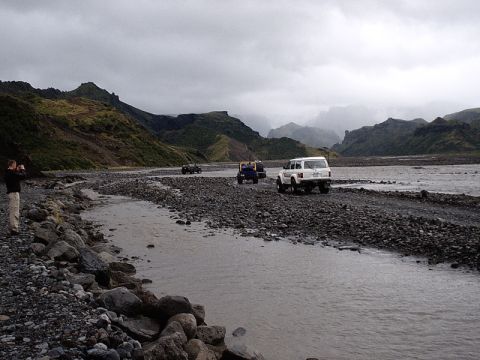 1996 Ford Bronco - Several SUVs traverse a rocky riverbed in a mountainous, overcast landscape.