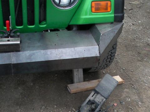 1987 Suzuki Samurai - Custom metal bumper on a green vehicle, showing part of the front end and tire.