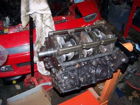 1991 Mitsubishi 3000GT - Engine block with crankshaft visible, part of a red vehicle in the background.