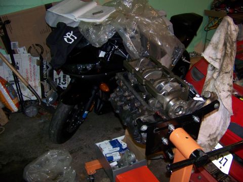 1991 Mitsubishi 3000GT - Engine assembly on a stand, with a black motorcycle partially visible behind it in a cluttered garage setting.