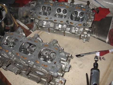 1991 Mitsubishi 3000GT - Two engine cylinder heads are laid out on a workbench, with tools nearby suggesting maintenance or repair work.