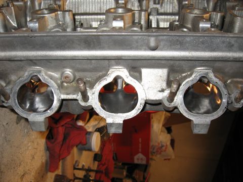 1991 Mitsubishi 3000GT - Close-up view of an engine's intake manifold, showing the ports for air intake. Background shows workshop items.