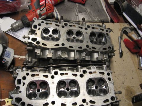 1991 Mitsubishi 3000GT - Engine cylinder heads are shown on a workbench, with tools like a drill and hammer visible.