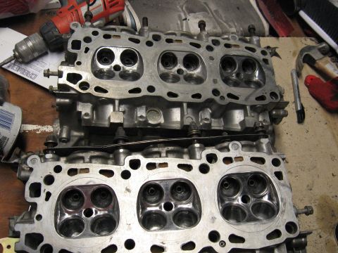 1991 Mitsubishi 3000GT - Close-up view of two engine cylinder heads, likely undergoing maintenance or repair, with tools visible in the background.