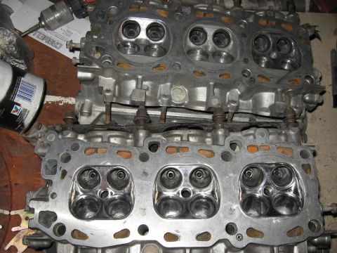 1991 Mitsubishi 3000GT - Two engine cylinder heads are shown, with a drill and can in the background.
