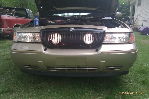 2000 Mercury Grand Marquis - Front view of a 2000 Mercury Grand Marquis, hood up, with a red pickup truck behind it.