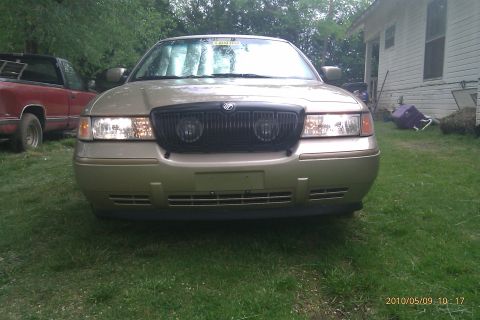 2000 Mercury Grand Marquis - A gold 2000 Mercury Grand Marquis is seen from the front, parked on a grassy lawn next to a white house.
