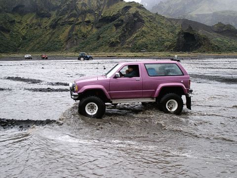 1996 Ford Bronco - Off-road vehicle navigates a rocky riverbed with mountains in the distance.