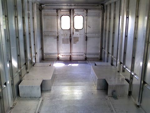 1989 Ford Bronco - The interior of a cargo van shows metal walls, double rear doors, and two built-in benches.