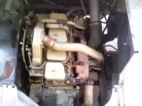 1990 Ford Bronco - Overhead engine-bay view of a tan/cream painted inline diesel engine with three rocker-cover access plates, a rusty red exhaust manifold an…