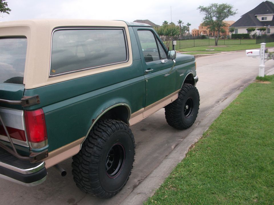 1989 Ford Bronco, green with tan top, lifted with large tires, parked on street