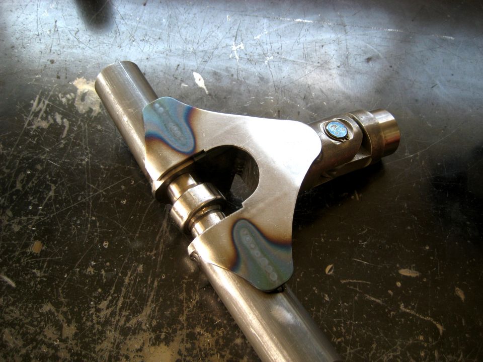 Metal part with welds and a u-joint, sitting on a scratched surface